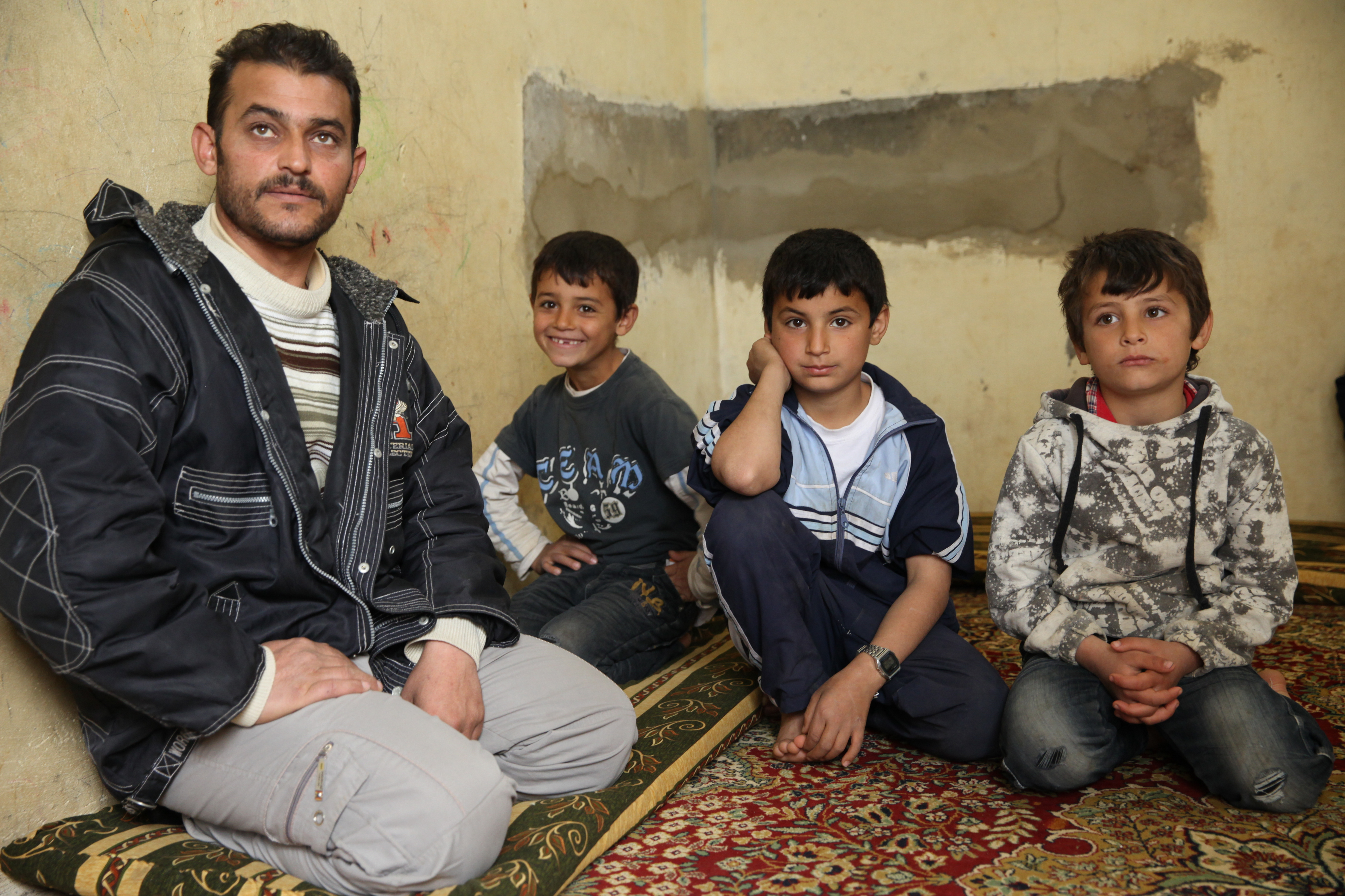 Abid, who fled to Lebanon from Syria one year ago, sits with four of his eight children in the cowshed they're now forced to call home.