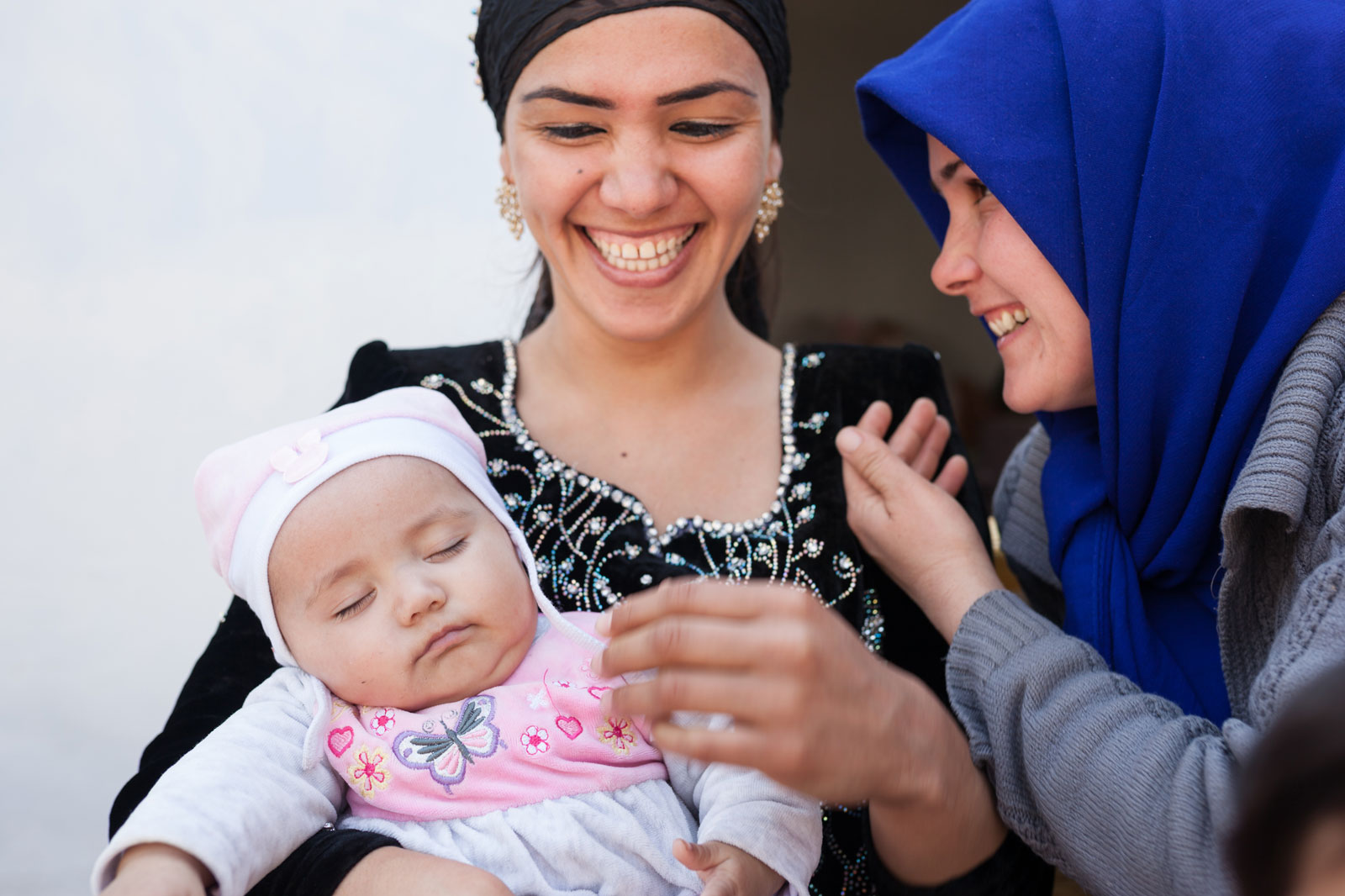 Two smiling women. The woman on the left is holding a sleeping baby.