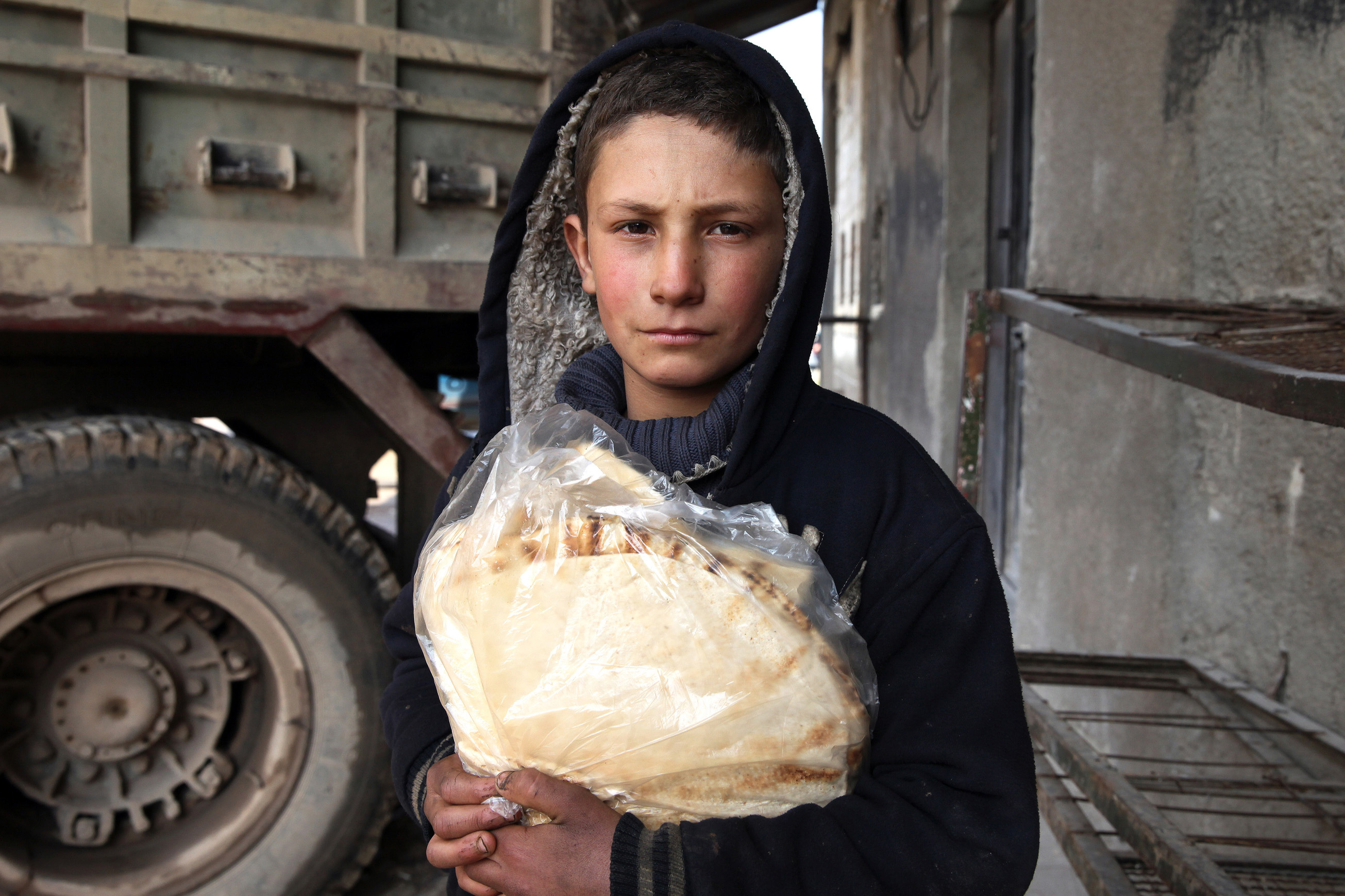 A boy wearing a black hooded sweatshirt holds bread in Syria