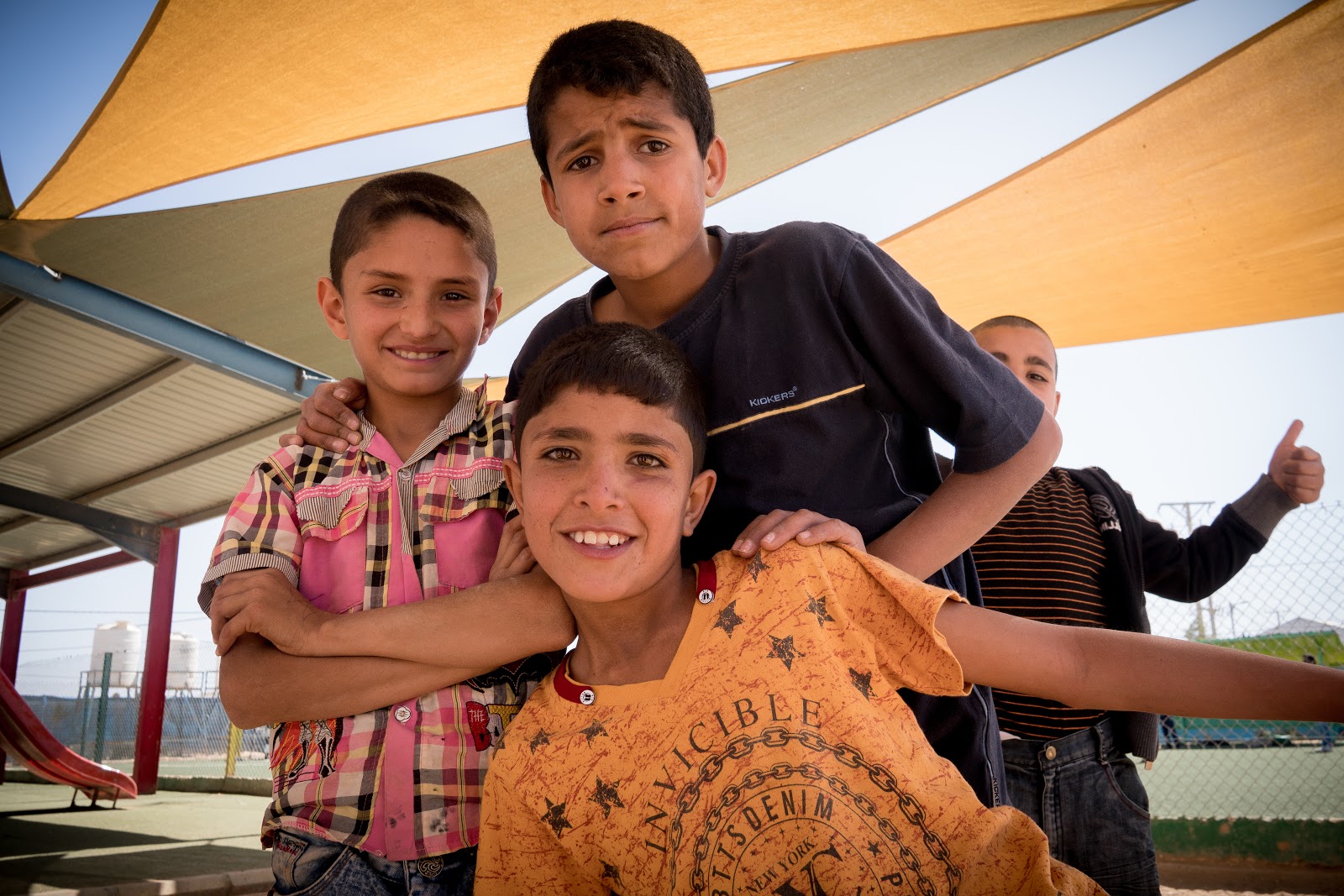 Four smiling young people gather for a group photo in a playground.