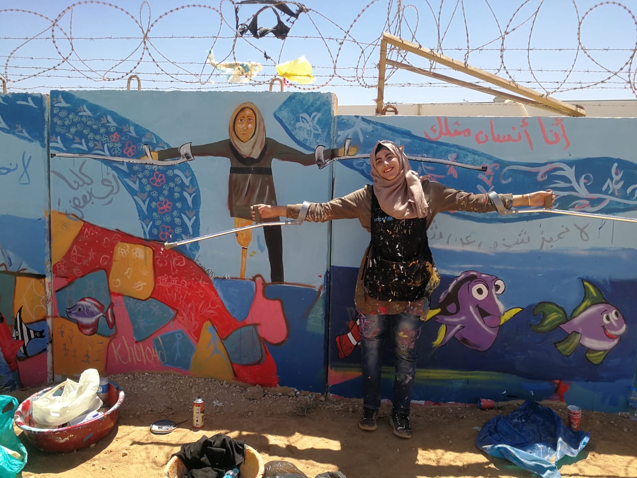 A young person poses in front of a mural of herself.