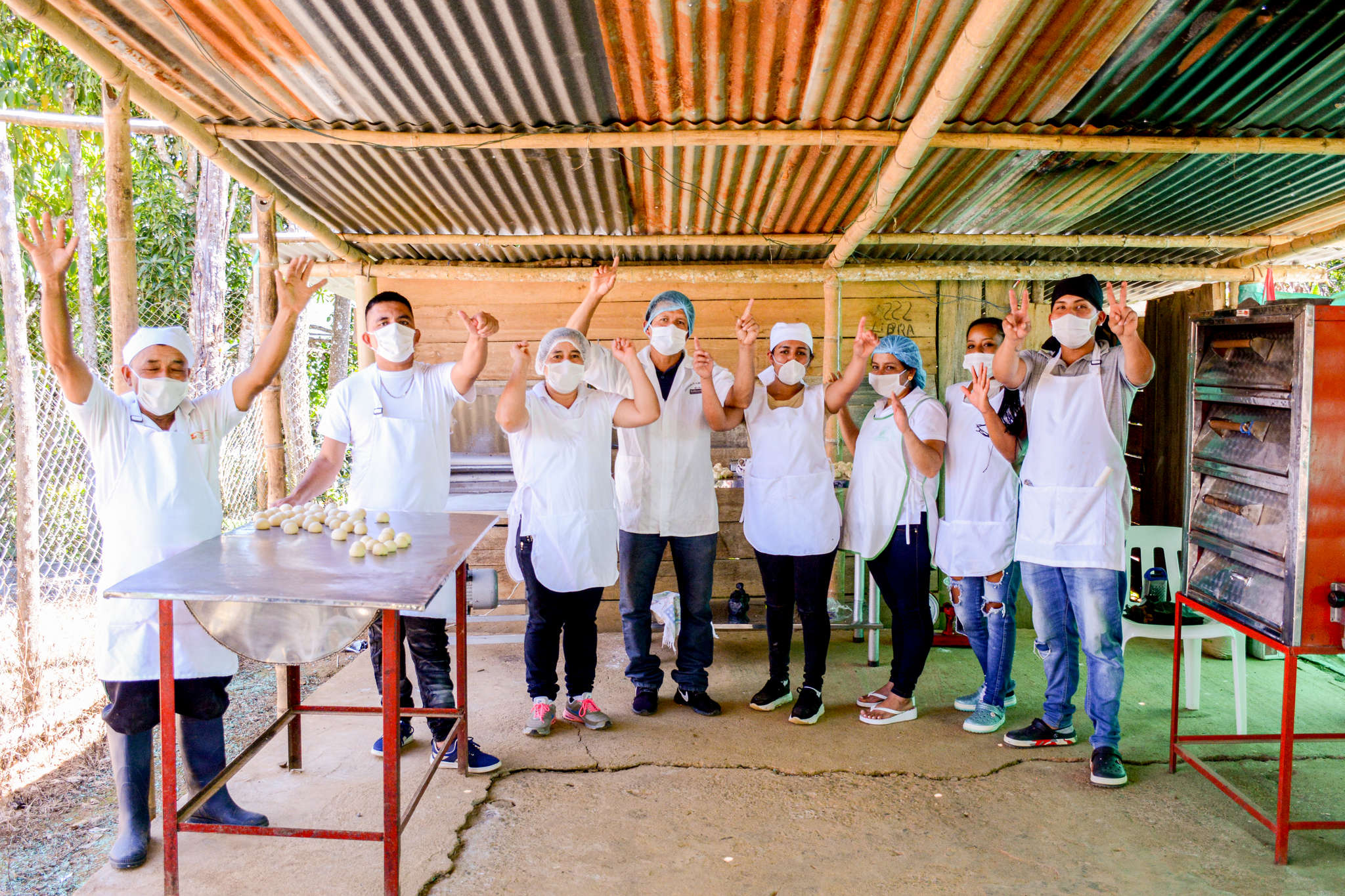 A group of bakers wave at the camera from an outdoor kitchen.