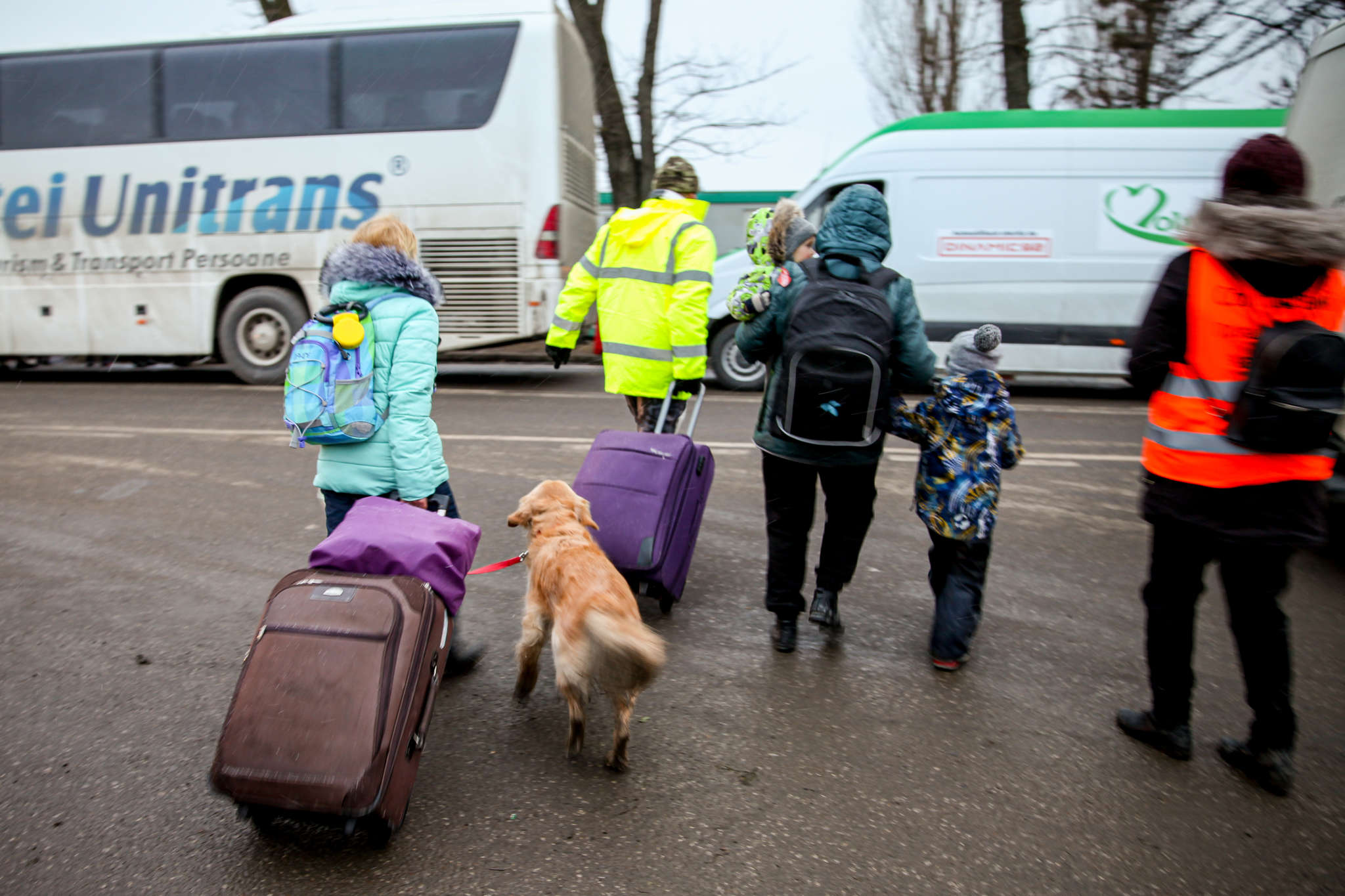 Emergency aid workers escorting women, children, and a dog to vehicles.