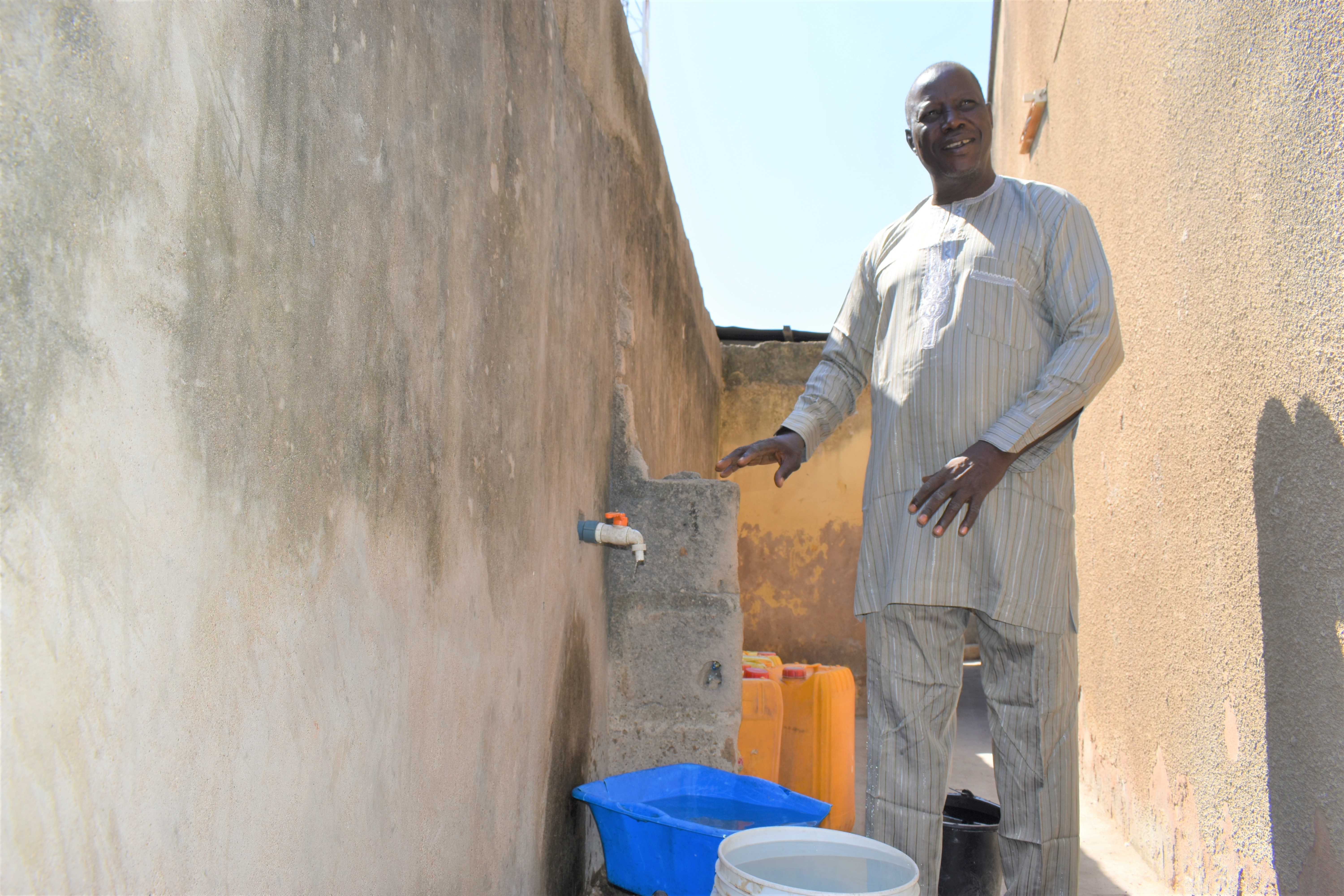 A person standing next to a tap in their compound connected to the local water facility.