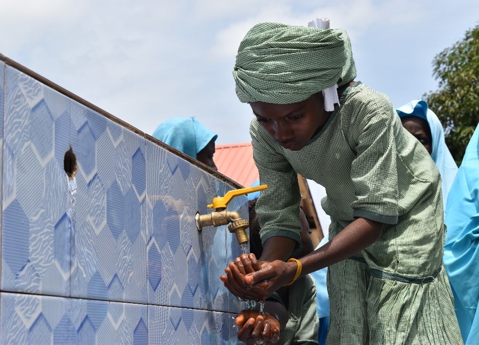 A young person washing their hands from a spigot.