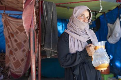 Syrian woman standing in tent with pitcher of water.
