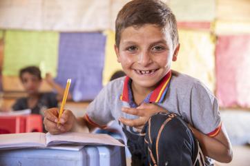 A smiling child seated with a book and pencil
