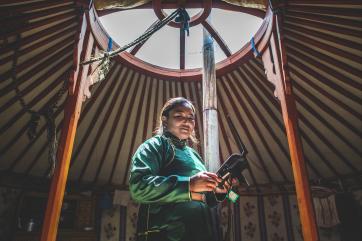 Altan stands in a yurt holding a device used to receive weather reports
