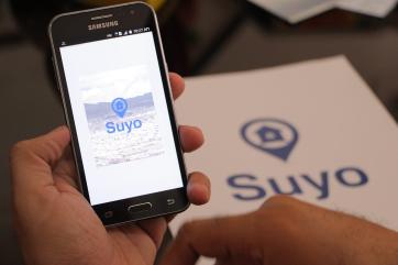 Hands holding a phone with the word "suyo" on the screen