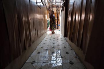 Carmen stands at the end of a tiled hallway that is soaked with water.