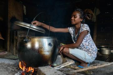 A girl in timor-leste cooks a meal in a large pot over a fire.