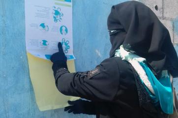 Muslim woman reviewing covid-19 prevention tips poster.