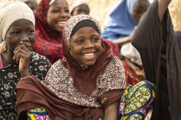 A teenager smiles and laughs while learning in a group of their peers.