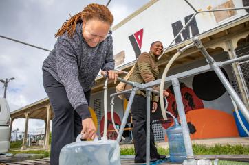 A person fills a vessel with water from a mercy corps water point outside the ymca.