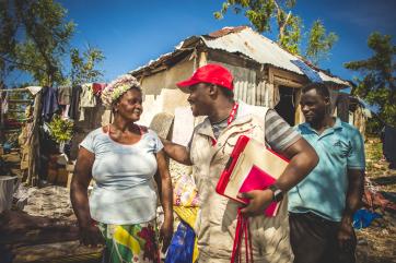 A mercy corps staff member consoles a person in front of their damaged home in haiti.