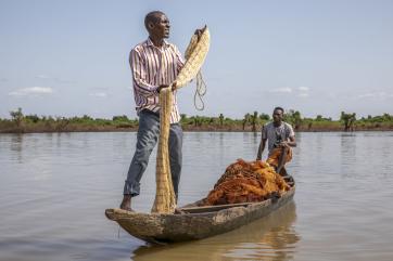 An adult manipulates a fishing net while standing on a boat in a river in nigeria.