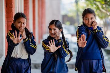 Three nepalese girls pose with hands out in front of them.