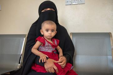 A person sits with a young child. 