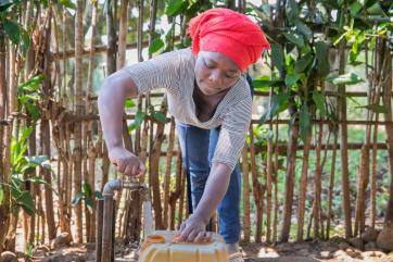 A farmer gets water from a mercy corps water tap near their home.