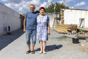 Ukrainian man and woman stand, arm in arm, among their farm warehouses.