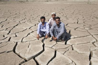 Three pakistani men crouch on dry, cracked earth.