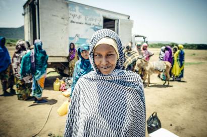 A woman in a headscarf smiles for the camera at a milk sale in ethiopia. 