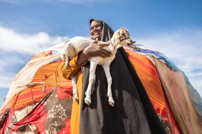 A person standing outside a temporary shelter while holding a small goat.