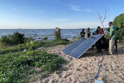 On the shore of lake victoria, mercy corps team members measure the power generated from solar panels during the installation of a pilot pump in musoma, tanzania.