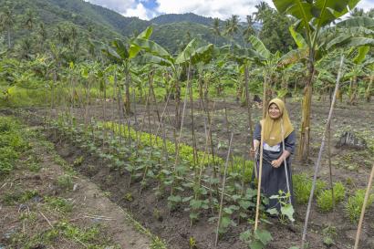 Indonesian woman in field with with hand tool, smiling.
