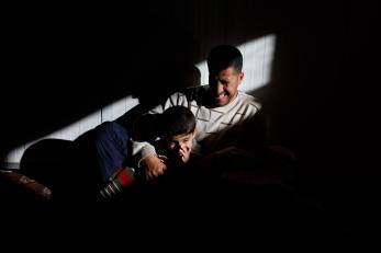 Ibrahim laughing with his 7-year-old son, khalil. they are in a beam of light that is piercing an otherwise dark room.