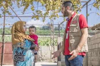 Maram is pictured holding a baby, speaking to a mercy corps employee