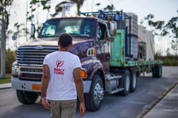 A man in a mercy corps t-shirt faces a large truck which is loaded with supplies