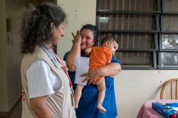 A woman holding a baby wipes away tears and smiles at a mercy corps team member in puerto rico
