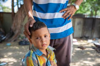 A young boy in colombia is comforted by a man's hand resting gently on top of his head