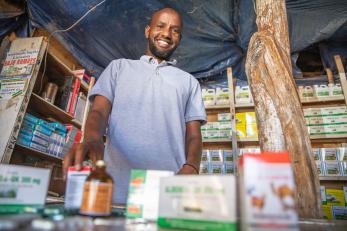 Abdikarim in his veterinarian pharmacy with shelves of medicine and supplies behind him
