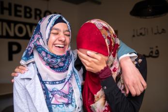Sisters in palestine laugh with arms around one another's shoulders