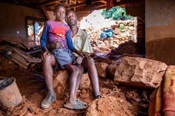 A father and his son sit together in their home, damaged from cyclone idai