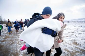 People moving across a cold landscape in serbia, holding a young child wrapped in a blanket
