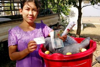 Myanmarese woman holding cash with red bucket.
