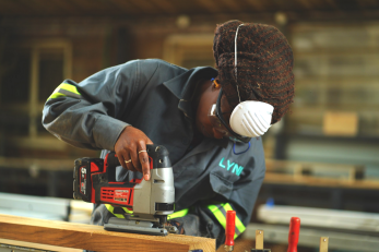 A person works with a power tool while wearing safety equipment.