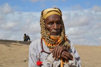 A elderly pastoralist wearing a headscarf leans on a stick in kenya.