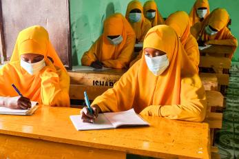School children sit study at their desks while wearing face masks.  