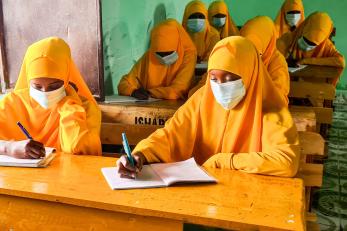 School children sit study at their desks while wearing face masks.
