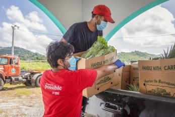Two mercy corps employees load a truck with food.