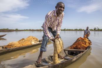 A fisherman manages a net while standing on a small water vessel.