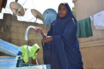 Na’ima fills a water drum with a hose connected to the tap in her compound.