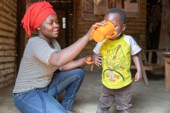 A farmer drinks water from a nearby mercy corps water tap with their 5 year-old son.