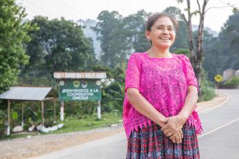 Guatemalan women stands smiling adjacent to roadside.