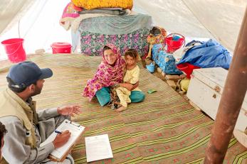 Pakistania mother and child sit in tent with mercy corps employee who is conducting interview.