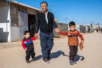 Abd al-kareem walks with his sons in jordan, za'atari camp